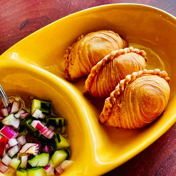 Three golden curry puffs and a side of cucumber and onion relish in a yellow serving dish.