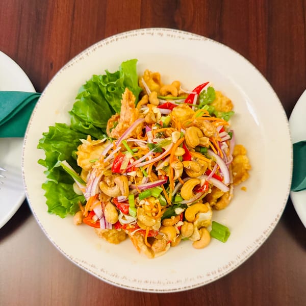 Crispy chicken salad with cashews, red onion, carrots, and chili on a bed of lettuce.